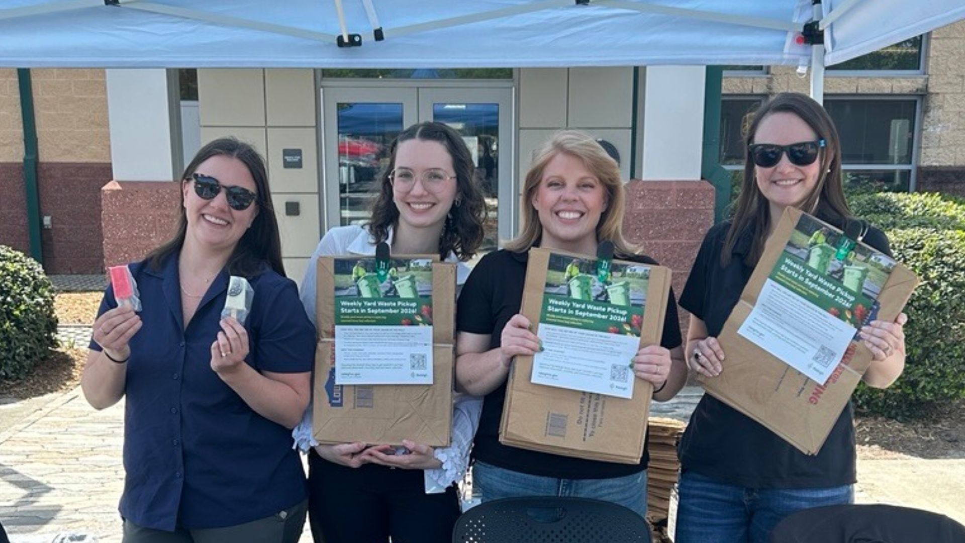 Three women hold biodegradable yard waste bags and one holds two popsicles
