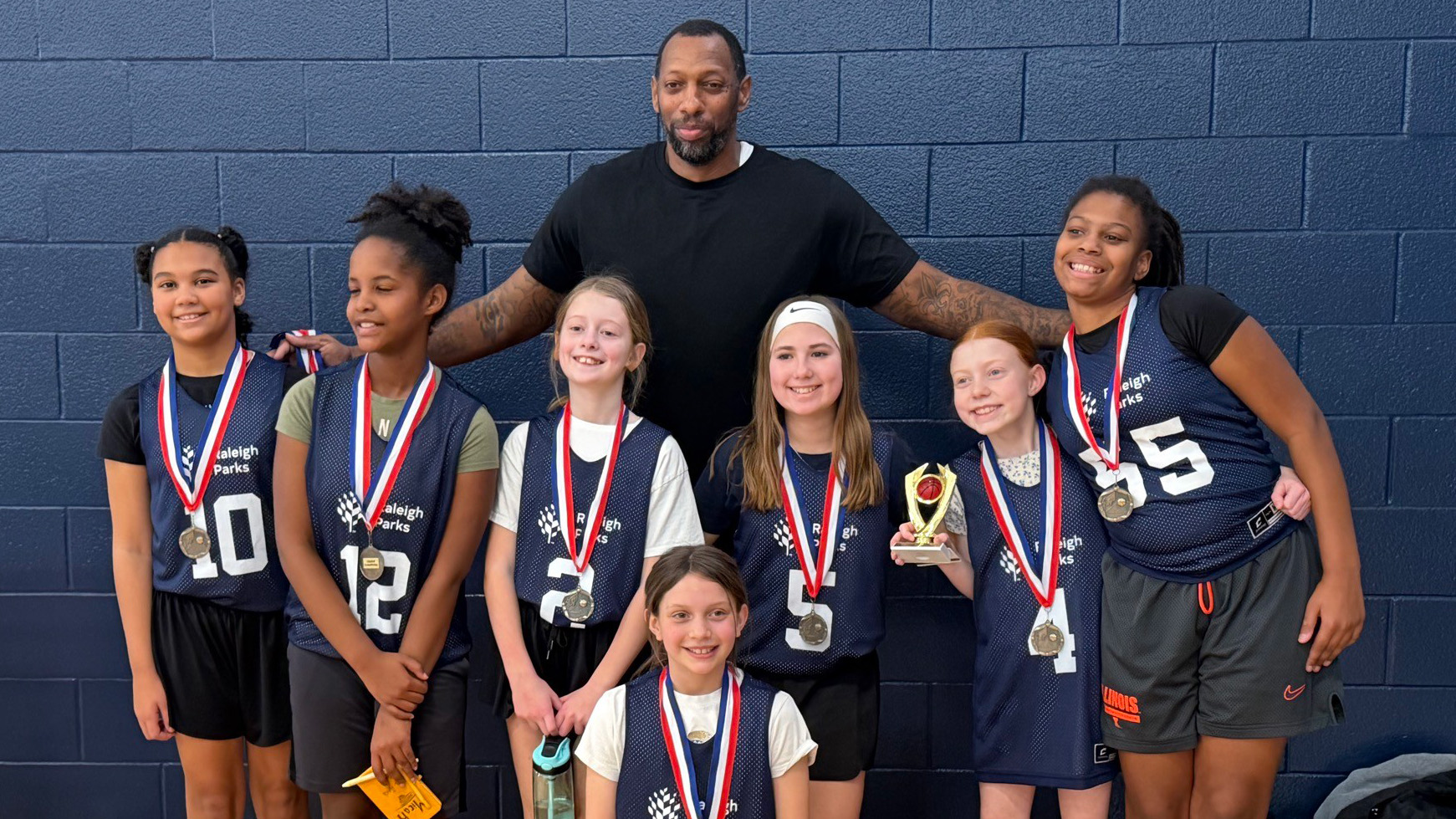 a group of smiling girls and their coach wearing championship medals
