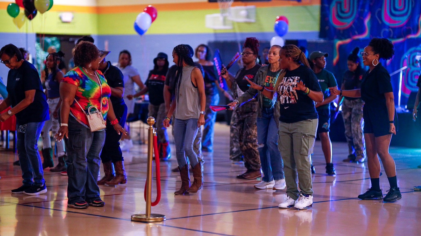 People dancing together at a colorful indoor community party with neon lights and balloons.