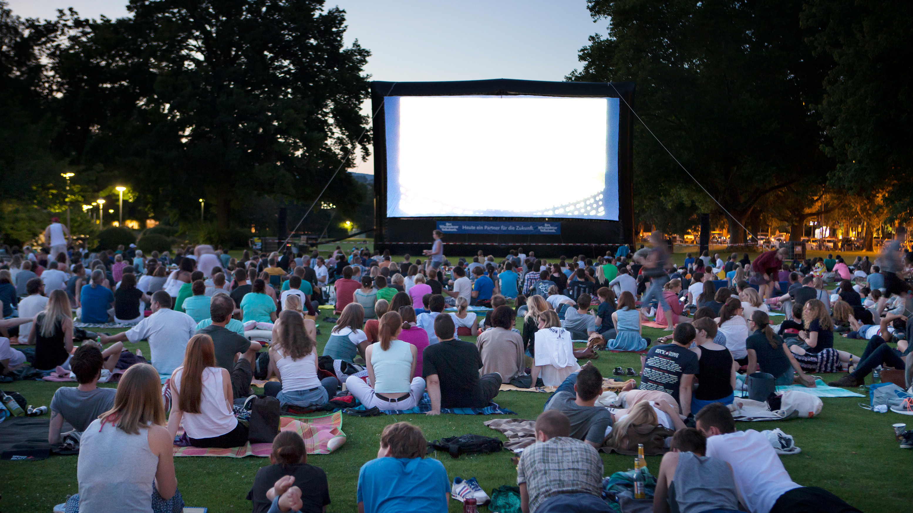 an outdoor movie event with people sitting on a lawn