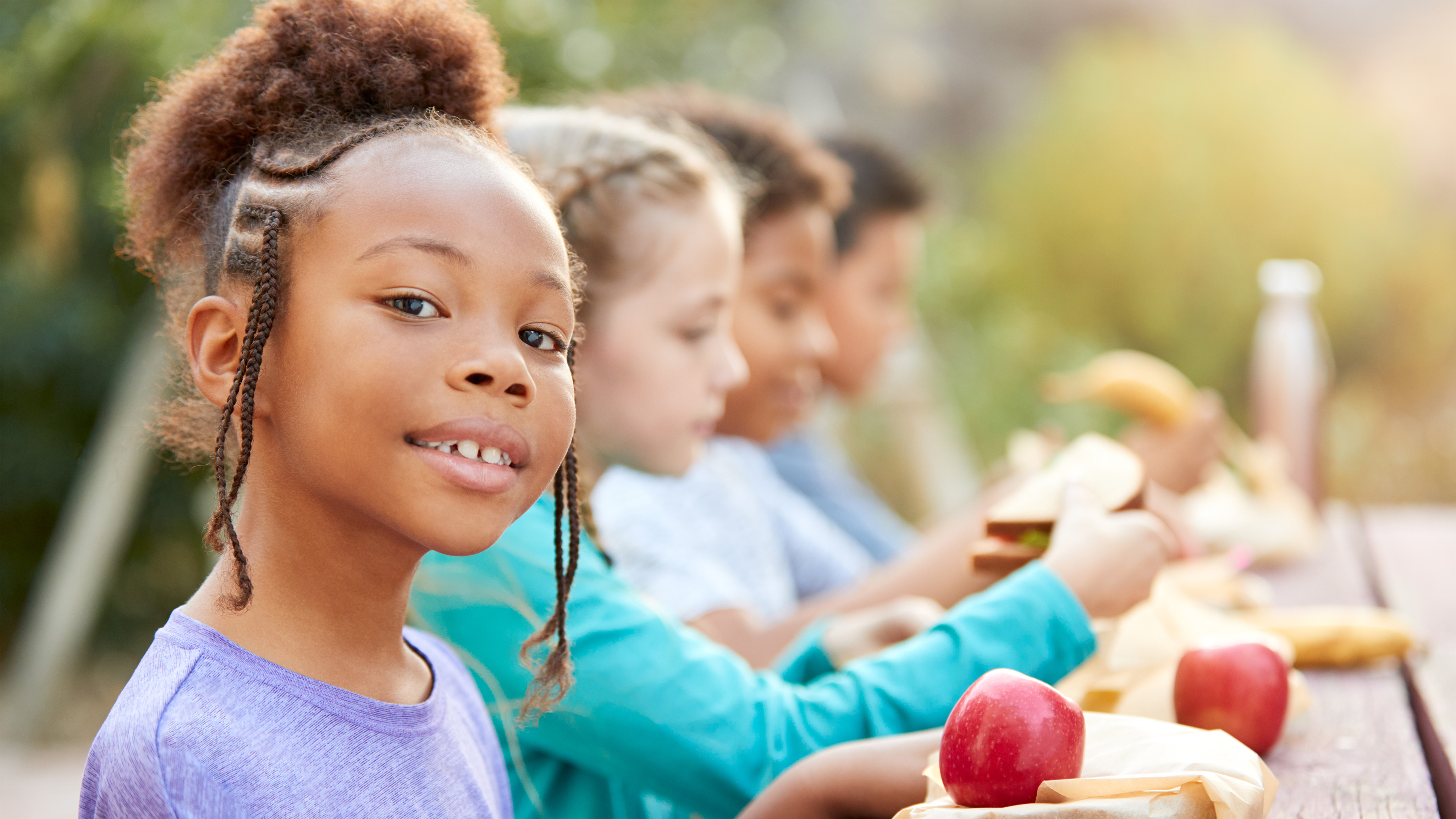 4 children sitting at a table outdoors enjoying food