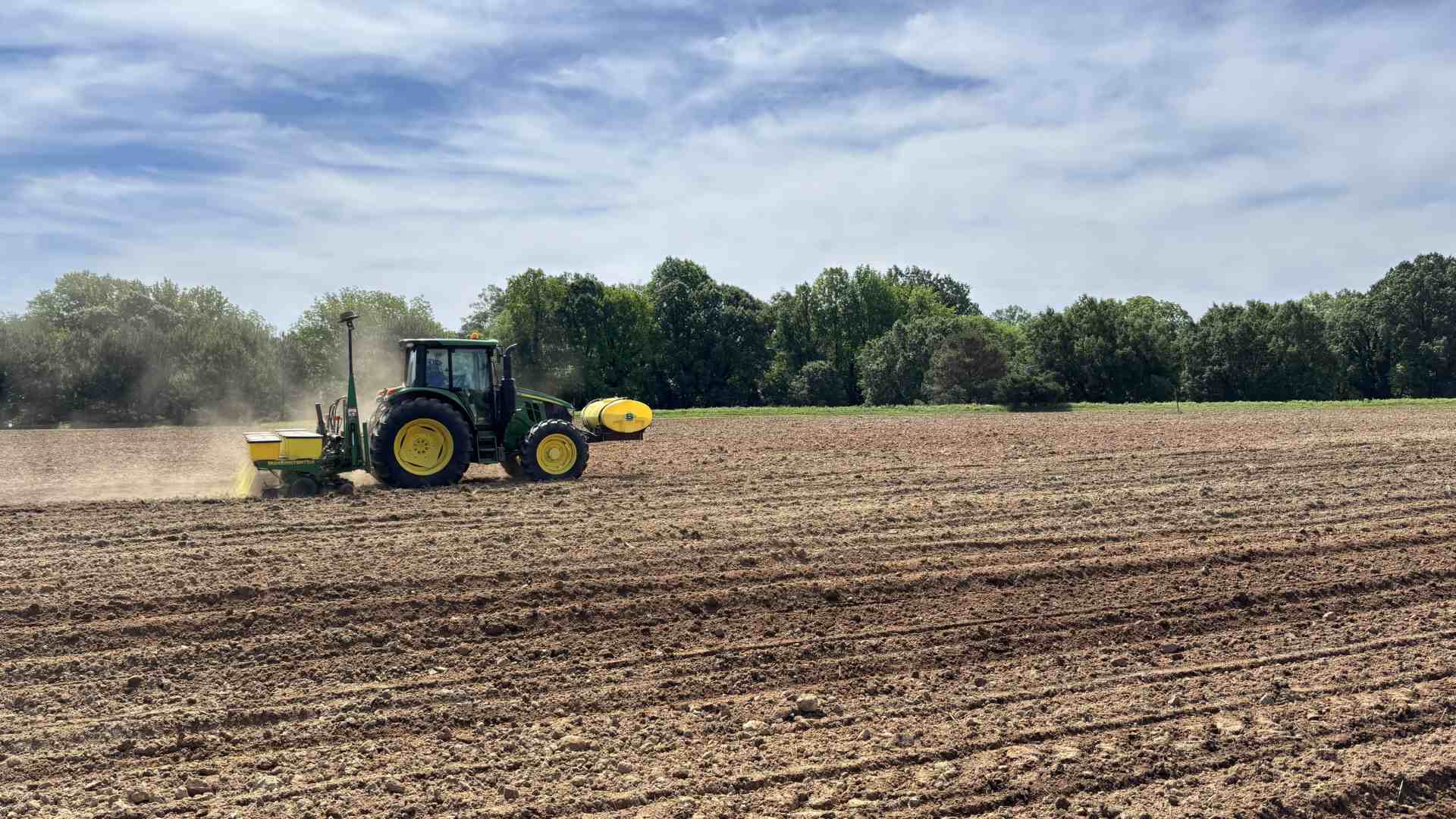 a tractor plowing a field with dust coming up behind it
