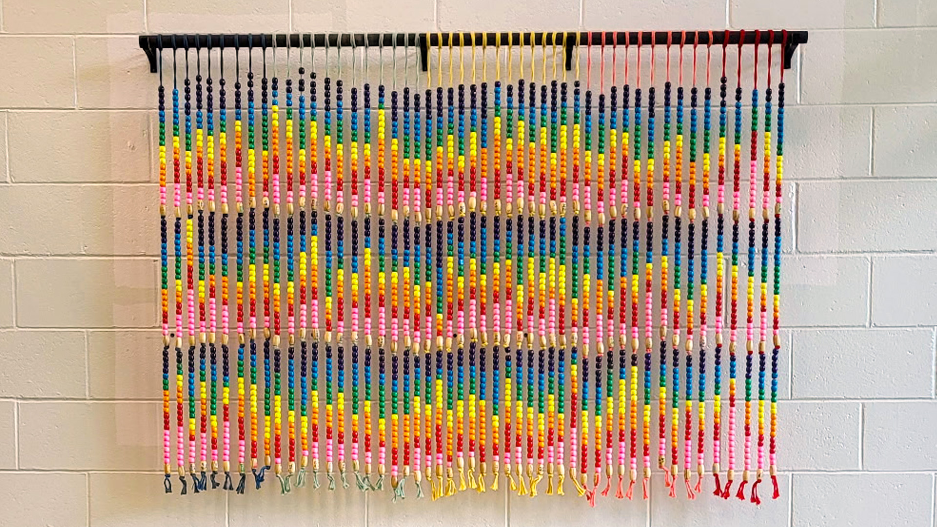 A wall hanging with many vertical rows of rainbow colored beads