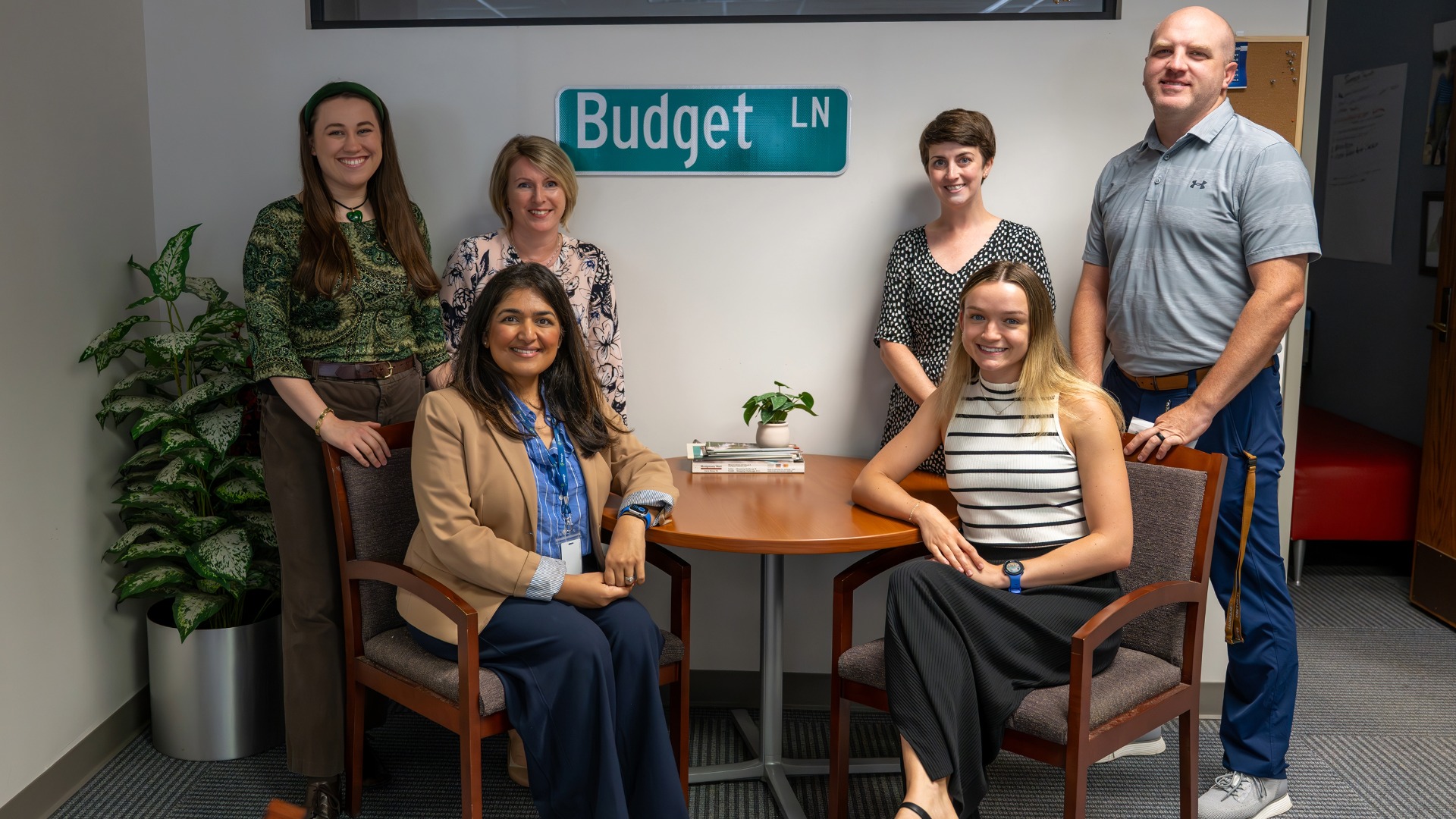 Five members of the Raleigh budget team with "Budget LN" street sign on the wall behind them