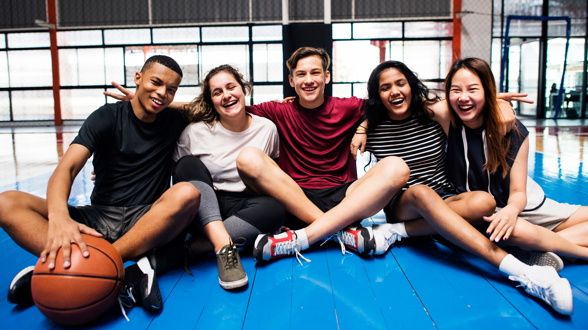 a group of teens, one with a basketball, smiling while sitting
