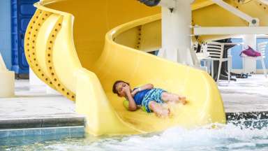 boy holding his nose going down a slide before hitting the pool inside the Buffaloe Road Aquatic Center