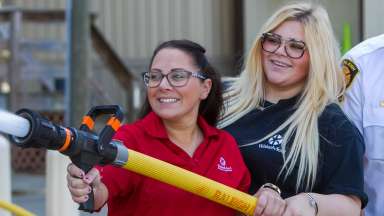 Two women holding fire hose next to firefighter