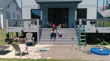 A drone still of a man dumping water on a child's head while sitting on steps