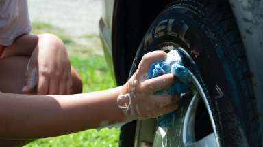 A person using a soapy cloth to wash a tire rim on the grass.