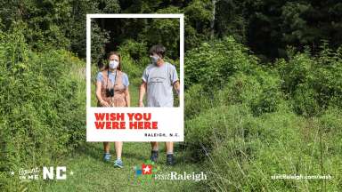 A man and woman walking in a grassy field wearing masks.
