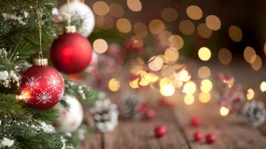 Holiday ornaments hung on the tree with defocused lights in the background