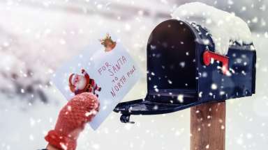 Hand wearing mittens putting letter to Santa in mailbox with snow