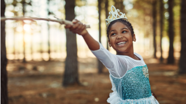 Little girl dressed in princess costume wearing crow waving wand