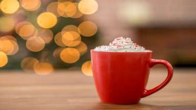 hot cocoa in red mug with whipped topping and holiday lights in background