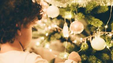 toddler putting an ornament on a lit Christmas tree