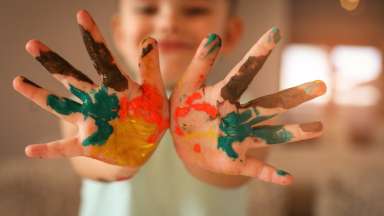 Kid holding hands up to camera covered in paint