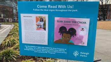 Story walk sign with cover of book and short description in Moore Square