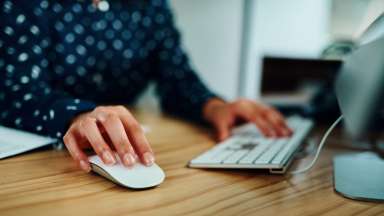 Woman sitting at computer with one hand on mouse and one on the keyboard