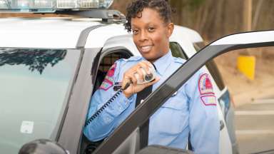 Female police officer standing outside a police vehicle using a handheld mic