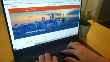 hands typing on a laptop with Raleigh website on the screen