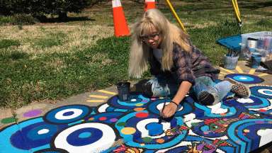 A young female artist painting a multi-color mural on a storm drain.