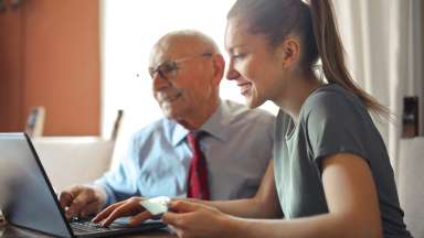 Woman and senior man use laptop computer together