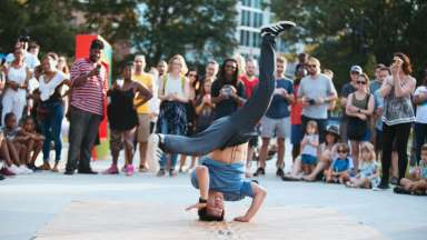 Man breakdancing spinning on head with legs in the air with people watching in a circl