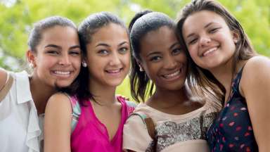 A multicultural group of four teenage girls smiling at camera
