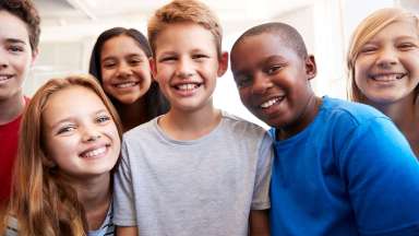 A multicultural group of six middle-school students smiling at camera