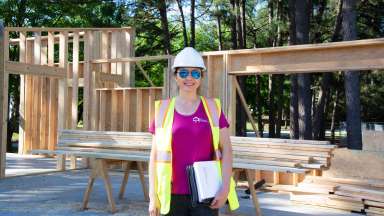 Woman in safety vest and hard hat holding clipboard smiling