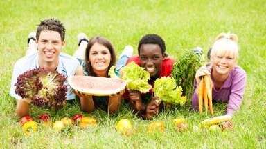 Four multicultural teens outdoors on grass holding up food items and smiling