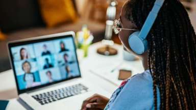 Woman with blue headphones looking at laptop with video chat