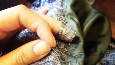 A hand is sewing two fabrics together while wearing a thimble