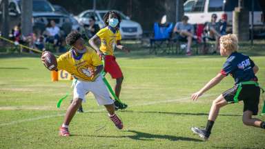 Two boys playing flag football.  One boy about to pass the ball while the other attempts to pull off a flag.