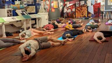 Group of 12 adults lying on the floor in a relaxing yoga pose in the museum.