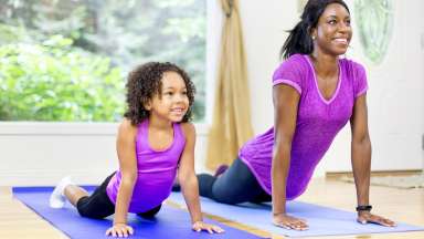 A mother and her daughter pushing up from the floor in a yoga pose.