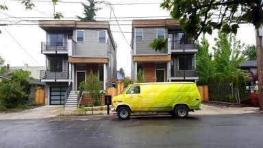 Two 3 story homes with yellow van parked out front on the street.