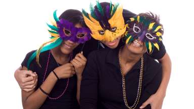 Three adults wearing mardi gras masks and smiling.