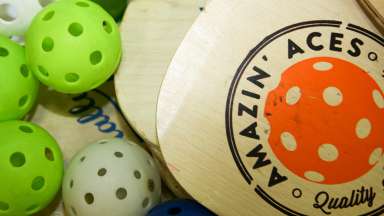 Two wooden pickle ball paddles surrounded with pickle ball balls.