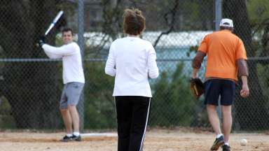 A woman beginning a pitch to a man standing ready to with a bat to swing at the softball.