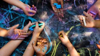 Several children's hands drawing with chalk on concrete.