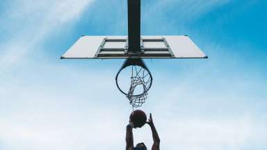 Low angle view of a young adult man scoring a goal in a basketball court. Sky in the background.