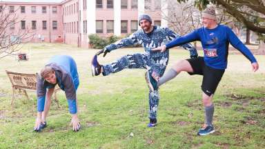 3 men wearing silly clothes stretching in preparation for a 5k run.