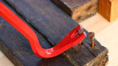 Deconstruction of building materials using a red crowbar to remove nails from old wood.