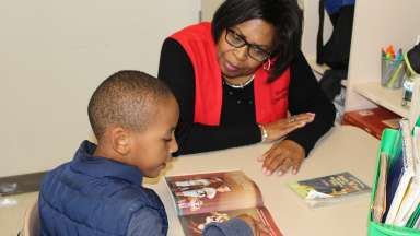 Foster Grandparent Program volunteer helps elementary student read a book.