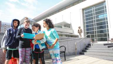 Four children studying a notebook outside a museum.
