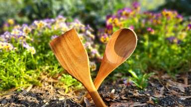 Wooden serving utensils stuck in the garden forming an "X".