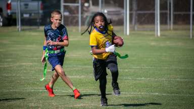 One boy running to make a touchdown being chased by an opponent.