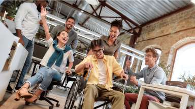 Group of enthusiastic young people, including man in wheel chair, collaborating in a work environment