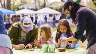Two young girls working on a craft with their fathers during a festival.